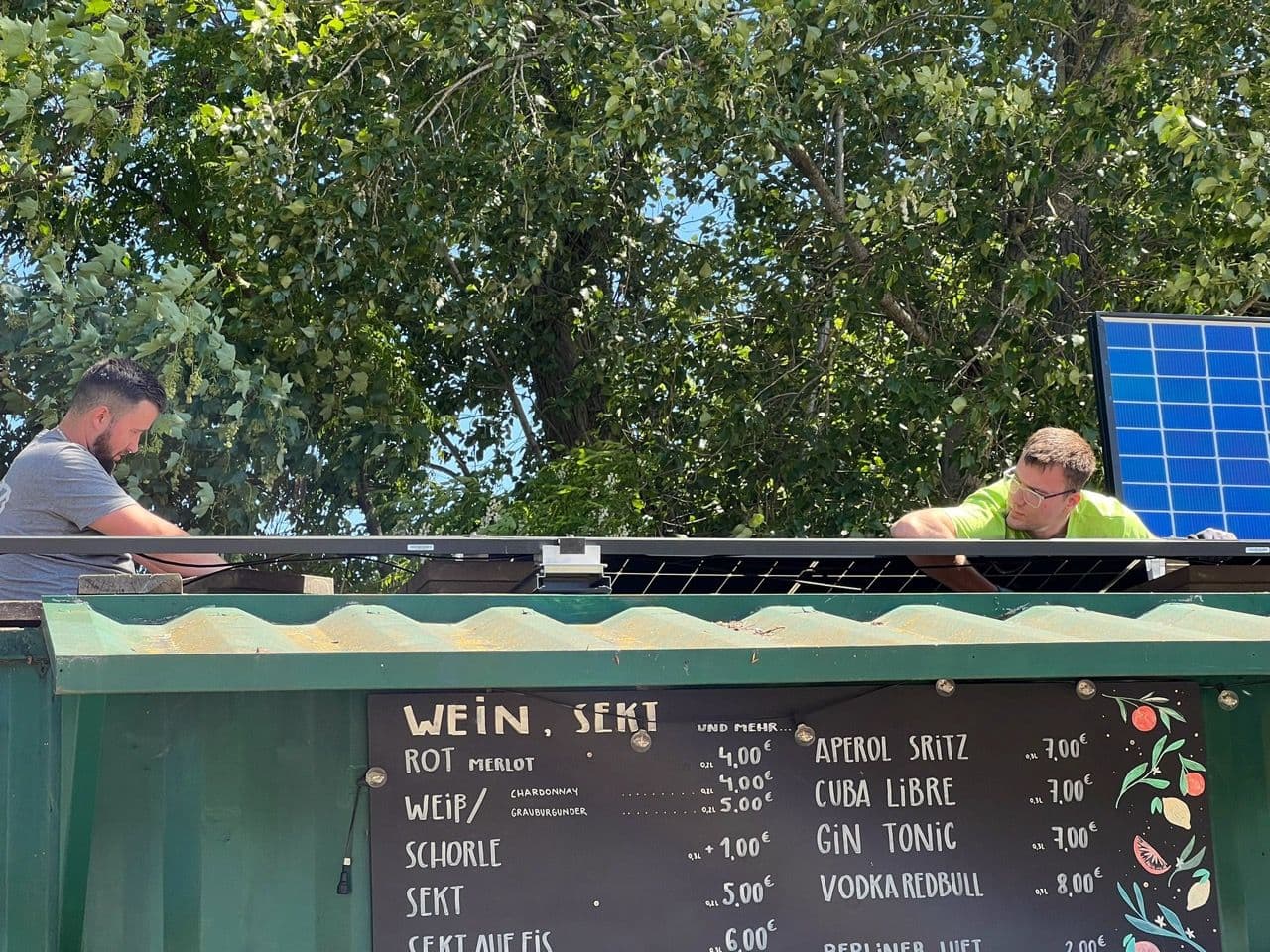 Auf dem Containerdach einer Bar arbeiten zwei Mitarbeiter der Solarfirma sunday solar an einer Photovoltaikanlage.